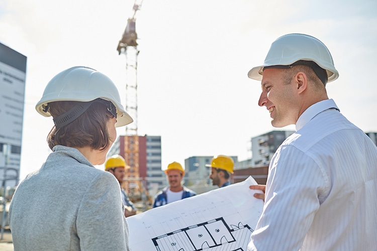 construction, architecture, business, teamwork and people concept - happy architects with blueprint at building site